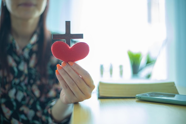 Croce di legno e cuore rosso in mano femminile con il concetto di amore e religione