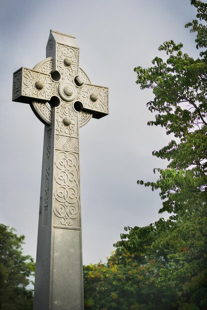 Croce di pietra celtica nel parco vicino a alberi verdi contro un cielo blu su un buio