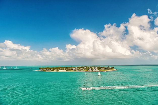 Crociera su barche turistiche o yacht che galleggiano sull'isola con case e alberi verdi su acque turchesi e cielo nuvoloso blu, yachting e vita sull'isola intorno alla bellissima Key West Florida, Stati Uniti
