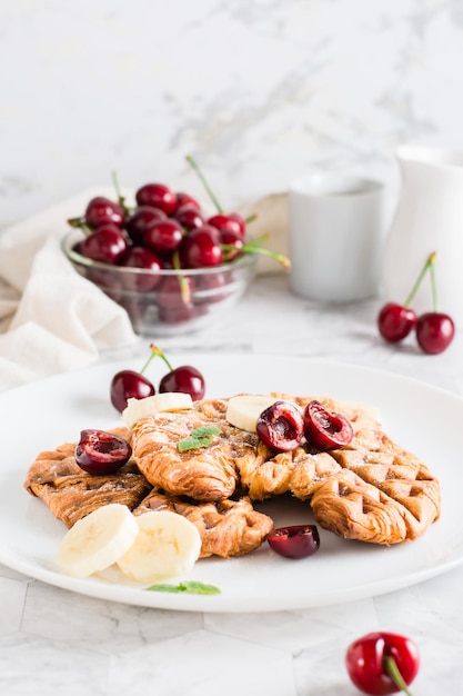 Croffles appetitosi con ciliegie e banane su un piatto sul tavolo Cibo di strada Vista verticale