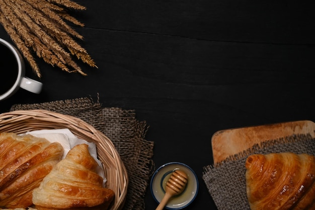 Croissant al burro fatto in casa appena sfornato in cesto di vimini decorato con grano sul tavolo di legno nero