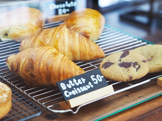 Croissant al burro fatto in casa e biscotti con etichetta nera in vetrina al negozio di panetteria.