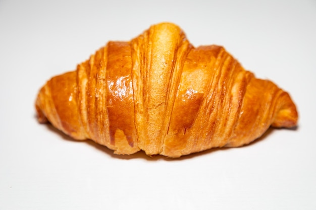 Croissant al burro marrone dorato con ombra isolata sullo sfondo semplice