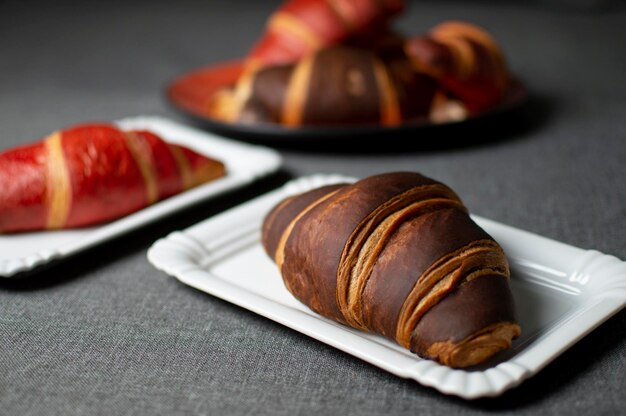 Croissant al cioccolato e rossi giacciono su piatti su un panno grigio closeup focacce