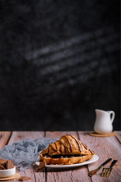 Croissant al cioccolato su un tavolo di legno, un bicchiere di cappuccino o caffè, deliziosa colazione