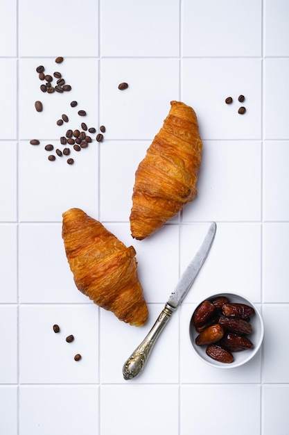 Croissant al forno cremosi al burro caldo adagiati su piastrelle bianche in ceramica quadrata sullo sfondo del tavolo vista dall'alto piatto con spazio per la copia per il testo