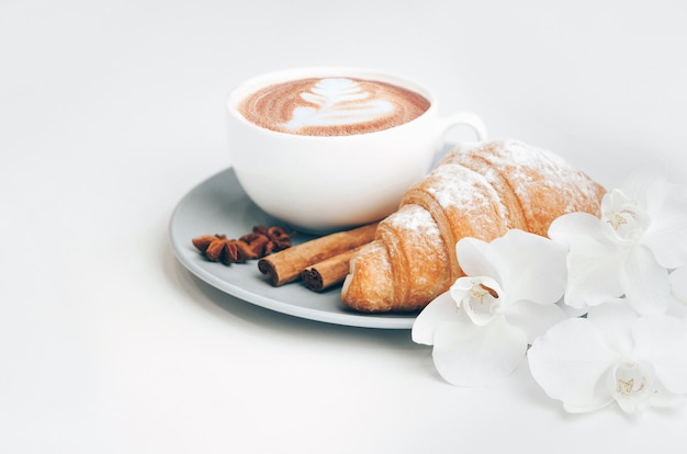 Croissant al forno fresco con la tazza di caffè e l'arte del latte, cannella