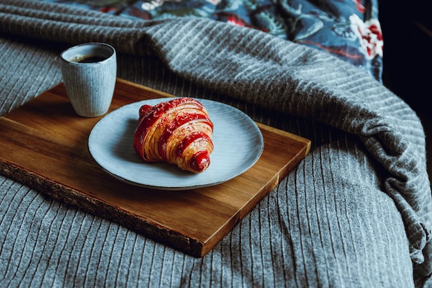 Croissant alla ciliegia con una tazza di caffè espresso su un vassoio di legno in un letto