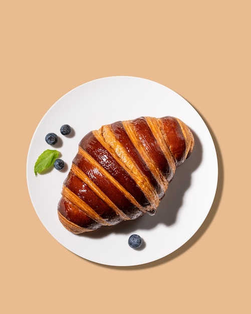 Croissant appena cotto su un piatto bianco e mirtilli su uno sfondo giallo Il concetto di una deliziosa colazione fatta in casa Vista superiore e spazio di copia