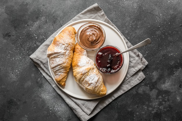 Croissant appena sfornati con marmellata di bacche su grigio scuro. Vista dall&#39;alto.