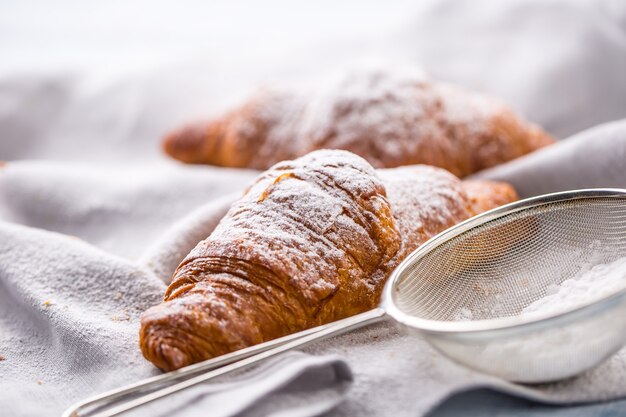 Croissant burrosi freschi cosparsi di zucchero in polvere sul tavolo della cucina.