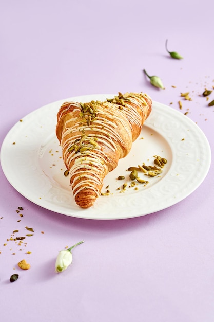 Croissant con crema di pistacchio e spolverata di noci su un piatto bianco su sfondo rosa