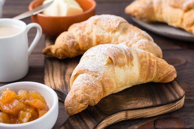 Croissant croccanti freschi, una tazza di caffè e marmellata in una ciotola su una tavola di legno sul tavolo. Brunch e pausa caffè