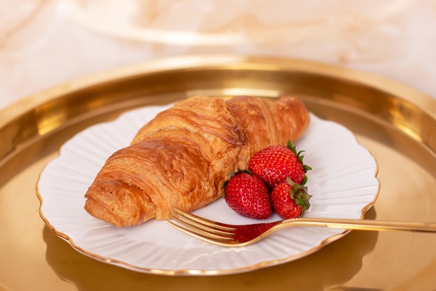 Croissant dolce con fragole fresche su piatto dorato