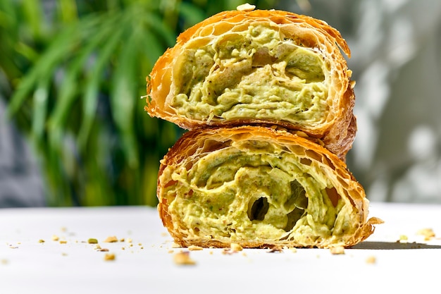 Croissant dolce con pasta di pistacchio e noci su un piatto bianco. Luce forte