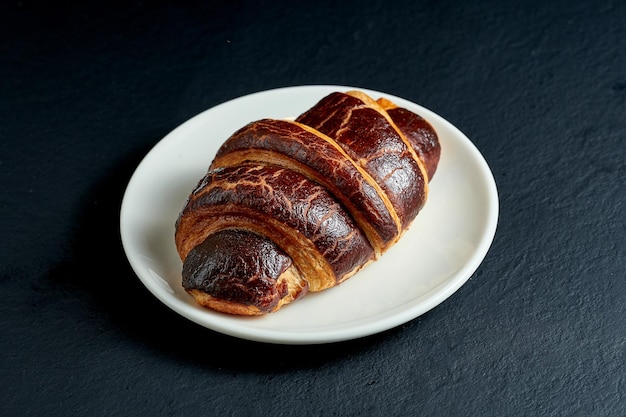 Croissant dolce cremoso con cioccolato in piatto bianco su sfondo nero