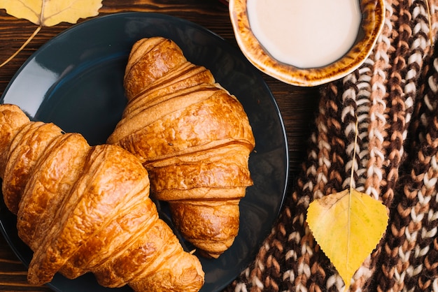 Croissant e bevanda del primo piano vicino a foglia e sciarpa