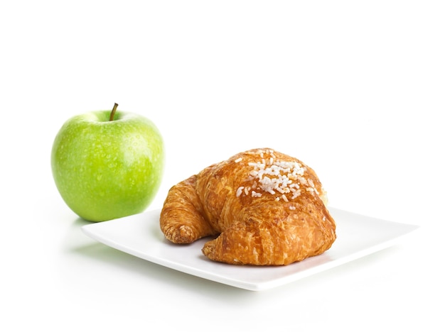 Croissant e mela verde isolati su bianco