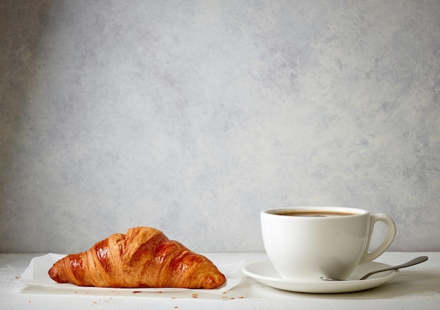 Croissant e tazza di caffè appena sfornati su tavola di legno bianca