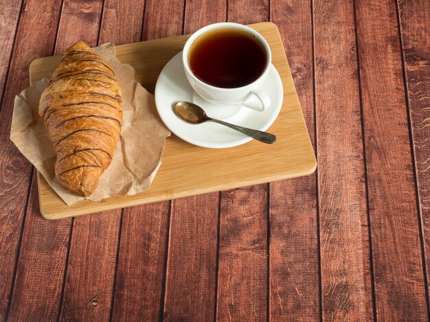 Croissant e tè della prima colazione su un tovagliolo del tessuto, superficie di legno scura