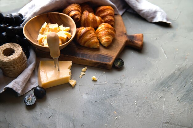 Croissant francesi gustosi originali con formaggio e uva sul tavolo di legno. burroso traballante pane viennoiserie caratteristica forma a mezzaluna. Formaggio in ciotola, coltello, tagliere come sfondo.