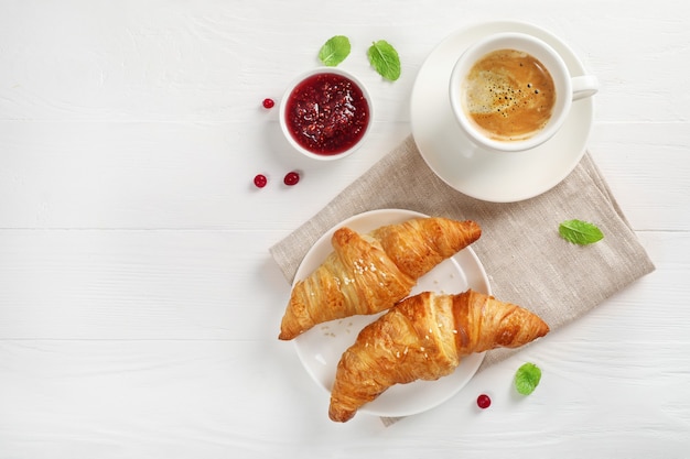 Croissant freschi, caffè nero e marmellata su legno bianco