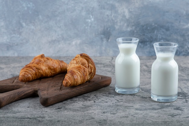 Croissant freschi e gustosi con brocche in vetro di latte poste sul tavolo in pietra.