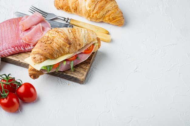 Croissant freschi sandwich con prosciutto, formaggio e foglia di insalata insieme, con erbe e ingredienti, su pietra bianca sullo sfondo, con copia spazio per il testo