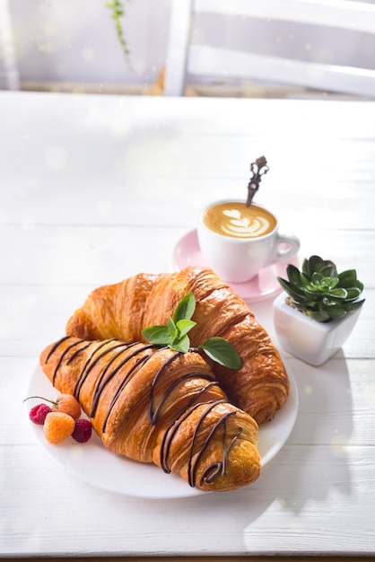 Croissant fresco con frutti di bosco e tazza di caffè per la colazione