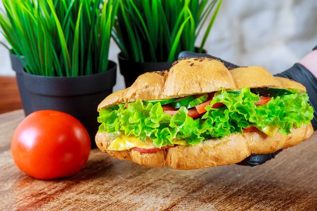 Croissant fresco con prosciutto e insalata nella mano di un cameriere in un guanto nero