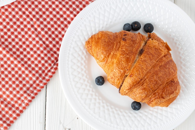 Croissant fresco decorato con frutti di bosco sul bordo di legno bianco, vista dall'alto