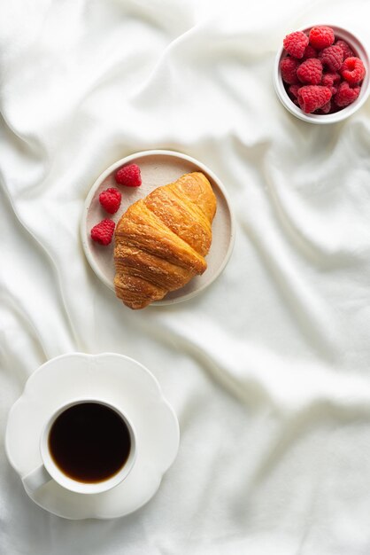 Croissant fresco e croccante con lamponi e una tazza di caffè