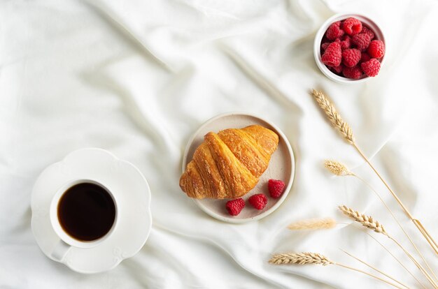 Croissant fresco francese con lamponi e una tazza di caffè sul letto