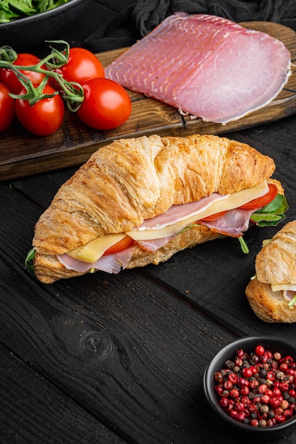 Croissant fresco o panino con insalata, prosciutto, jamon, set di prosciutto, con erbe e ingredienti, su sfondo di tavolo in legno nero, con spazio per la copia del testo