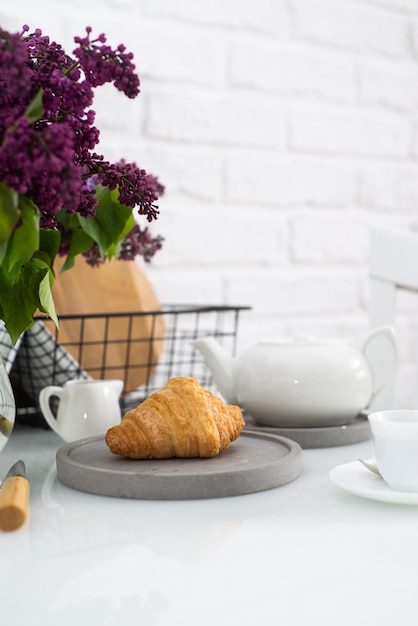 Croissant fresco su un piatto grigio su un tavolo con una teiera bianca e lillà