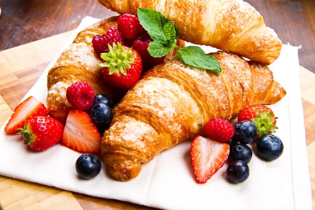 Croissant gustosi freschi con frutti di bosco su fondo di legno