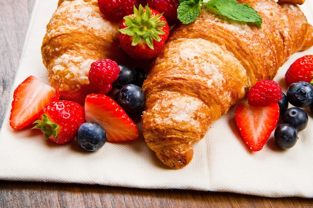 Croissant gustosi freschi con frutti di bosco su fondo di legno