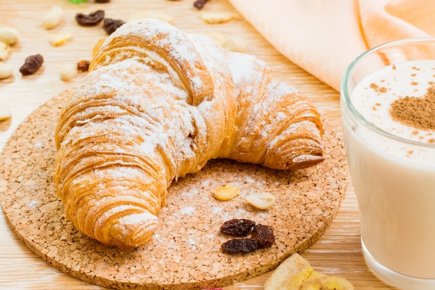 Croissant in zucchero a velo e bicchiere di latte con cuore da cannella su una tavola di legno