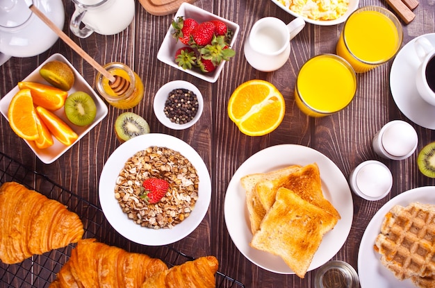 Croissant, muesli, toast, frutta, uova, cialde e tazza di caffè sullo sfondo. Concetto di colazione