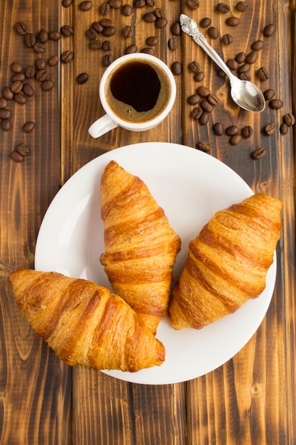 Croissant nel piatto bianco e caffè nero nella tazza sulla tavola di legno marrone. Vista dall'alto.