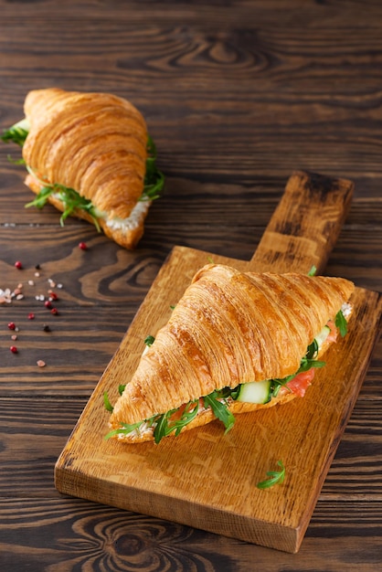 Croissant panini con formaggio cremoso di salmone e rucola su una tavola di legno Orientamento verticale.