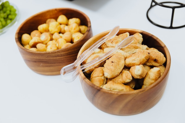 Croissant piccoli, gustosi e croccanti si trovano in un piatto di legno. In cima al piatto ci sono delle pinze per loro.