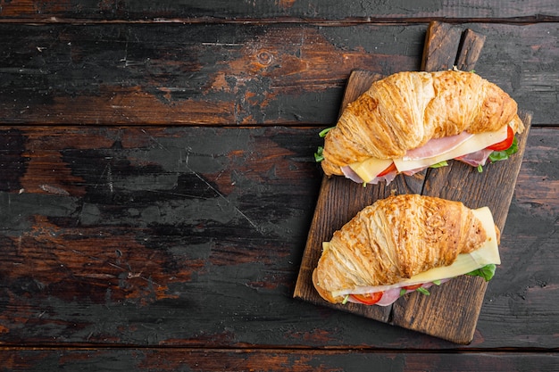 Croissant sandwich con prosciutto, pomodori, formaggio set, sul vecchio legno scuro dello sfondo della tavola, vista dall'alto laici piatta, con copia spazio per il testo