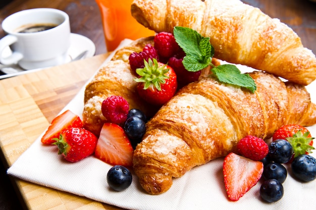 Croissant saporiti freschi con le bacche su fondo di legno