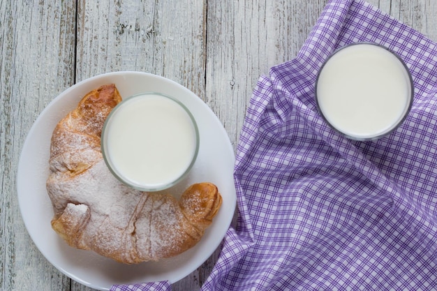 Croissant sul piatto con latte sul vecchio tavolo di legno per la colazione sfondo