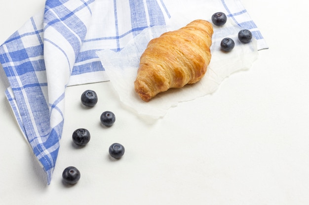 Croissant sul tovagliolo a quadretti bianco e blu. Mirtilli sul tavolo.