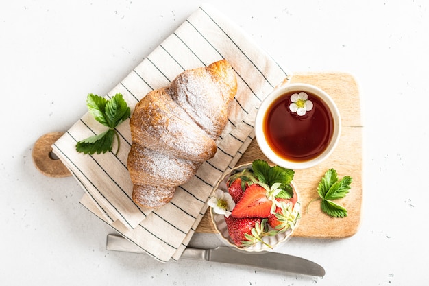 Croissant, tè e fragole. Concetto di colazione, mattina e primavera, vista dall'alto