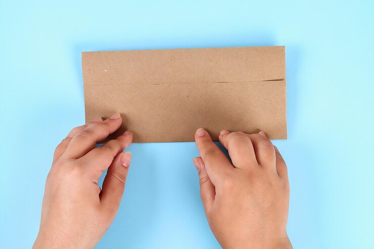 Photo cropped hands of person folding paper against blue background