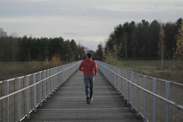 Cross country jogging in campagna uomo in felpa arancione che attraversa il ponte di legno nella nazione