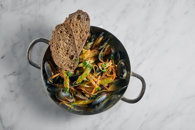 Crostacei Cozze Vongole con verdure e crostini di pane in padella di rame su marmo bianco